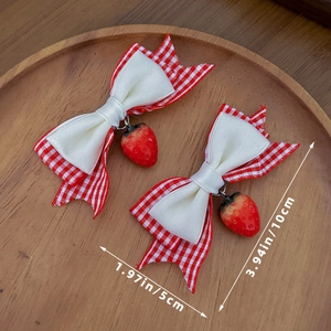 Detail von Lolita-Haarspangen mit roten Karo-Schleifen und Erdbeeren auf Holztablett
