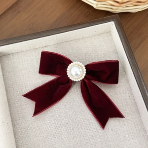 Detail of burgundy velvet bow hair clip with central pearl and golden accents on a tray