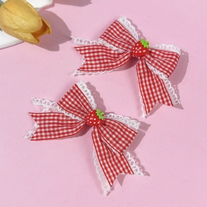 Dettaglio di fermagli per capelli con fiocchi scozzesi rossi e ciondoli a fragola