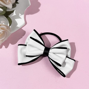 Detail of white faux leather bow hair tie with black piping on pink background