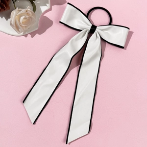 Detail shot of white leather bow hair tie with black contrast edges on pink background