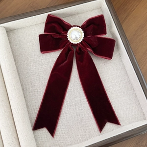 Detailed view of a burgundy velvet bow hair clip with a vintage pearl center on a beige tray