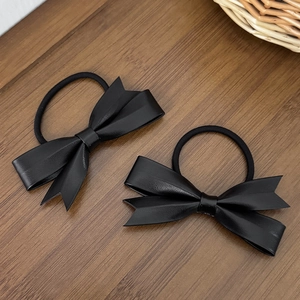Deux élastiques à cheveux avec nœuds en similicuir noir sur une table en bois foncé