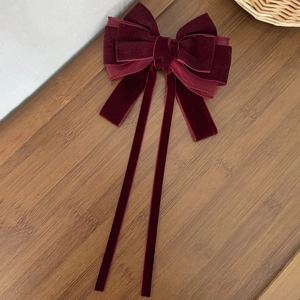 Elegant deep burgundy velvet bow hair clip with long ribbons on a rustic wood surface