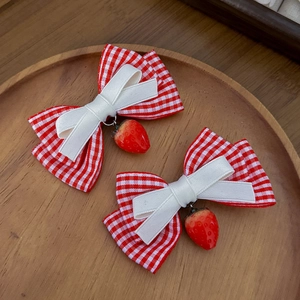 Detail von roten Karo-Schleifen mit Erdbeer-Anhängern auf einem Holztablett