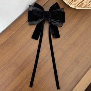 Detail of elegant black velvet layered bow hair clip with long ribbons on wooden surface