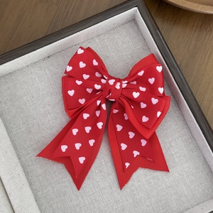 Detailed close-up of red grosgrain bow hair clip with pink heart patterns on a tray