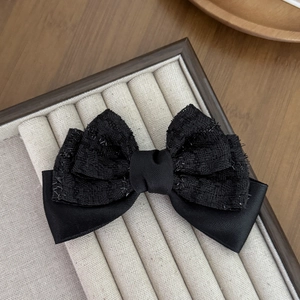 Détail de la pince à cheveux en tweed noir et satin avec des textures élégantes