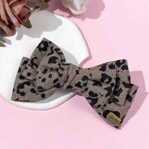 Detail of leopard print bow hair clip with gold Lucky metal tag on pink background