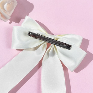 Elegant cream satin ribbon bow hair clip with silver metal alligator grip on pink background
