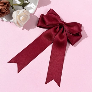 Detail of burgundy satin ribbon bow hair clip with elegant layered design on pink surface