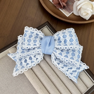 Close-up of blue ribbon bow hair clip with white lace mesh detail on display tray