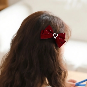 Detailed view of a burgundy velvet hair bow clip with heart rhinestone on a model