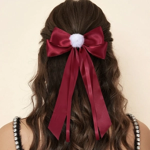 Detail of burgundy satin bow hair clip with white pompom and long flowing ribbons
