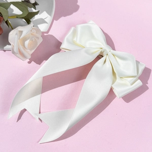 Detailed view of multilayer white satin bow hair clip with ribbons on a pink surface