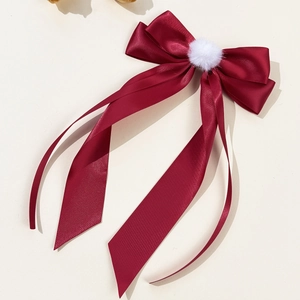 Close-up of elegant burgundy satin bow hair clip with a soft white pom pom and long ribbons