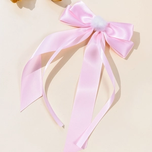 Close-up of pink satin bow hair clip with a soft white pompom and long ribbons