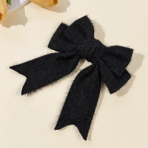 Detail of elegant black fuzzy faux mink bow hair clip with soft plush texture on beige background