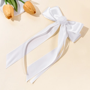 Close-up of white satin bow hair clip with plush pompom and long flowing ribbons