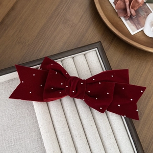 Close-up of burgundy velvet bow hair clip with sparkling rhinestones on beige velvet