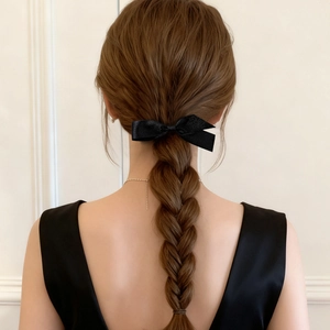 Detail of elegant black satin bow hair clip styled on a brown braided ponytail hairstyle