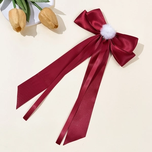 Detail of wine red satin bow hair clip with plush white pom-pom and elegant long ribbons