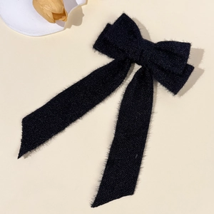 Detail of the soft black plush bow hair clip with long ribbons on a beige background