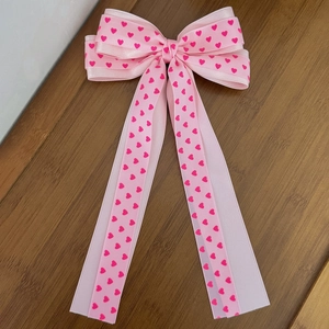 Detail der rosa Haarschleife mit Herzmuster-Bändern und langen Bändern auf Holz