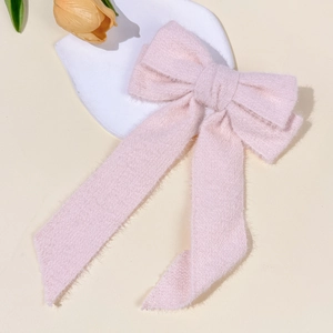 Detail of a soft pink fuzzy plush bow hair clip with ribbons on a decorative background