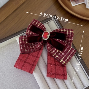 Close-up of wine red tweed and velvet bow hair clip with central ruby and gold accents