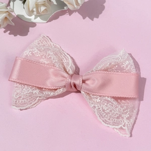 Close-up of pink satin bow hair clip with white floral lace layers and elegant texture