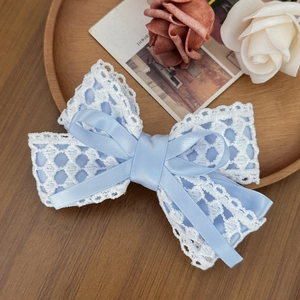 Elegant blue and white lace bow hair clip with hollow embroidery on a wooden tray