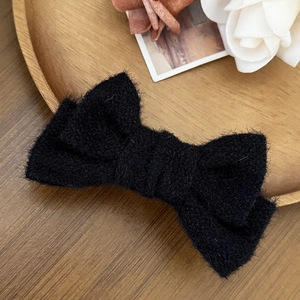 Dettaglio del fermaglio a fiocco nero in peluche con texture morbida su vassoio legno