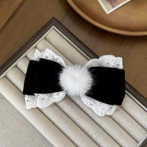 Detail of black velvet hair clip with white lace trim and a fluffy pompom accent