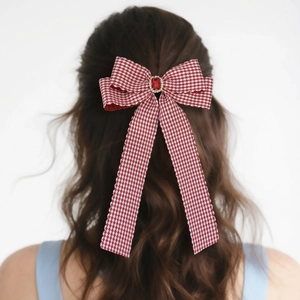 Detail view of red plaid bow hair clip with faux ruby gemstone on long ribbons