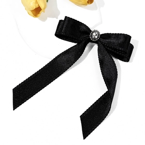 Detail of black satin bow hair clip with central sparkling rhinestone and long ribbons