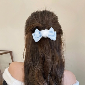 Blue bow hair clip with white pompom shown on dark wavy hair for styling reference