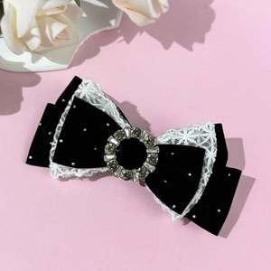 Detailed macro view of black velvet bow hair clip with white lace trim and rhinestones