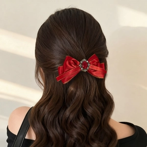 Detail view of a vintage red silk bow hair clip with ruby gemstone on wavy brown hair