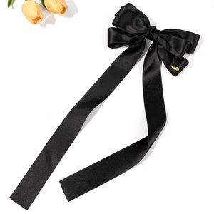 Détail d'un grand nœud à cheveux en satin noir avec rubans et logo métallique doré