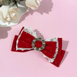 Close-up of red velvet bow hair clip with white lace trim and sparkling rhinestone center