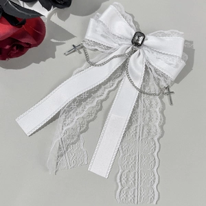 Détail d'une barrette nœud en dentelle blanche avec pierre noire et chaînes croix
