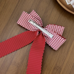 Elegant red and white houndstooth plaid bow hair clip with long ribbons on wood surface