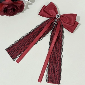 Macro detail of wine red satin bow with black lace, silver cross and heart gem