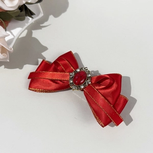 Macro shot of a red satin bow hair clip with vintage golden gemstone and rhinestones
