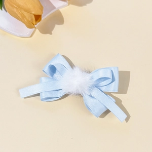Detailed view of light blue satin bow hair clip with a white fluffy pom pom accent