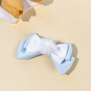 Close-up of blue and white satin bow hair clip featuring a fluffy white pom-pom detail