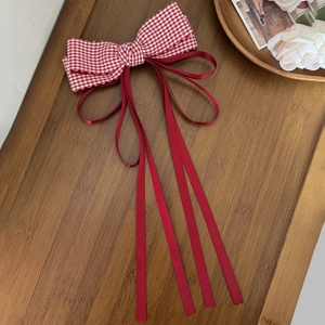 Close-up of red plaid bow hair clip with satin ribbons on a vintage wooden surface