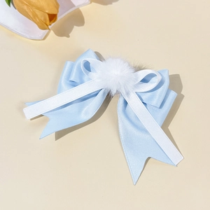 Detail of blue and white bow hair clip featuring a soft plush pompom and ribbon layers