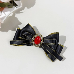 Detail of bohemian bow hair clip with black satin, gold trim and red gemstone